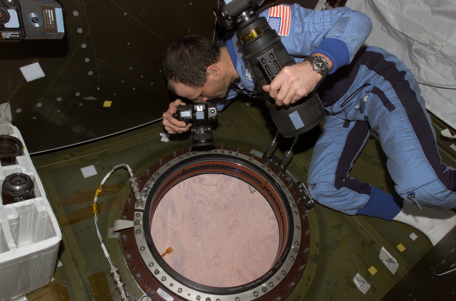 Don Pettit wearing his Omega Speedmaster using a still camera to photograph the topography of a point on Earth from the...