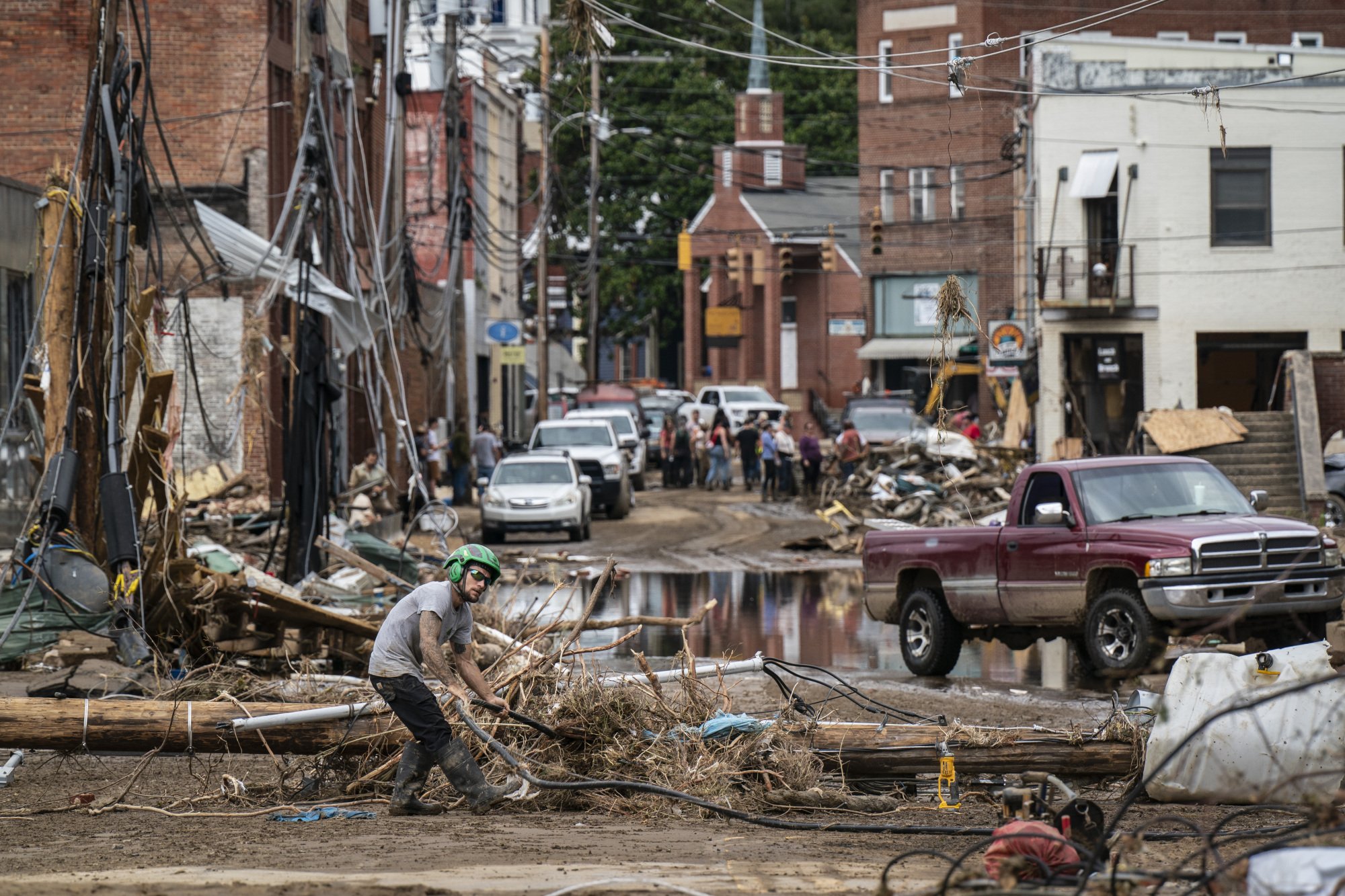 A man in a green helmet removes heaps of debris from a destroyed city street. 