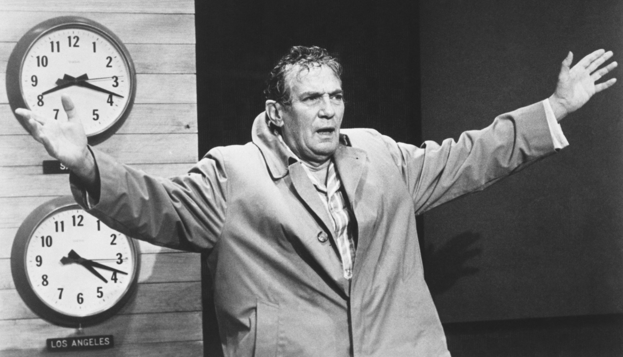 In Network, Howard Beale throws his arms wide in front of the clocks in his studio