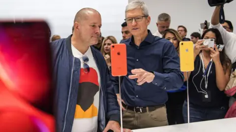 Getty Images Tim Cook, the CEO of Apple, and Jony Ive view an iPhone during an event in 2018.