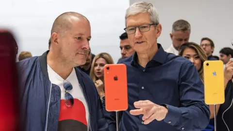 Getty Images Tim Cook, the CEO of Apple, and Jony Ive view an iPhone during an event in 2018.