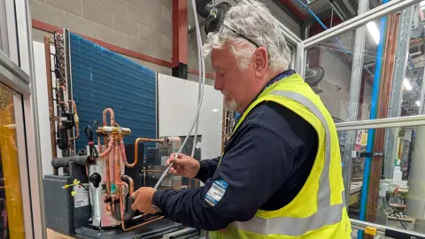 Chris Baraniuk A man in a hi-viz vest works on a heat pump