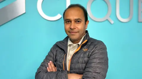 Cequence Security Wearing a puffa jacket and with his arms folder Shreyans Mehta stands in front of a blue background.