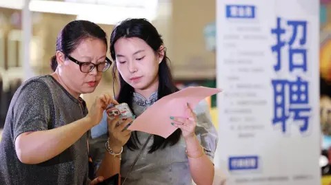 Getty Images The picture shows two women reading instructions on a mobile phone while at a job fair in China's Lianyungang City.