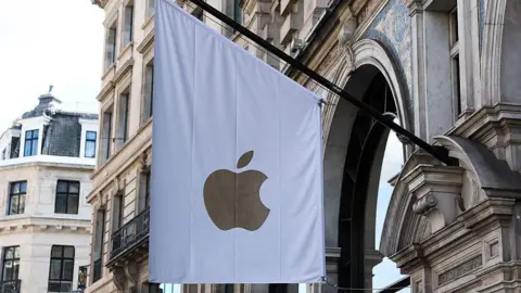 Getty Images A white flag bearing a gold apple logo hangs outside the stone front of an apple store