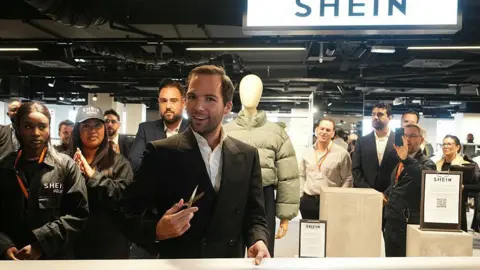 DIMITAR DILKOFF/POOL/AFP The director of the Bazar de l'Hotel de Ville (BHV) department store Karl-Stephane Cottendin prepares to cut the ribbon at the opening of Asian e-commerce giant Shein's first physical store at the BHV department store in Paris on November 5, 2025