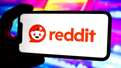 Getty Images A phone against a bright puple coloured background with a white screen and the orange Reddit logo on it.