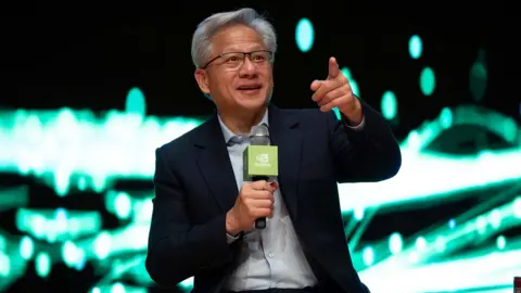 Getty Images Jensen Huang is speaking into a microphone and sitting in front of a bright green and white lit background 