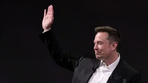 Getty Images Musk in a white shirt and black jacket with his hand raised