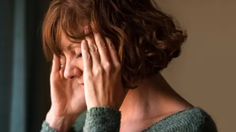 Getty Images A middle-aged woman holding her head