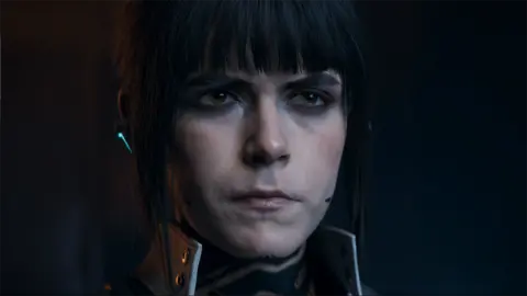 Activision Screenshot shows a photo-realistic rendering of Kiernan Shipka's character, dimly lit, with a stern expression on her face. She wears a high-necked jacket and an earpiece with a microphone stretching towards her mouth.