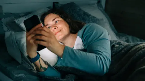 Getty Images Smiling woman using smartphone in bed at night