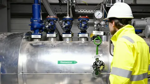 MVV Energie A large stainless steel pipe with four blue valves on the top and a gauge.