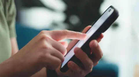 Getty Images A close up of the hands of a person using a smartphone. They are tapping something on the screen.
