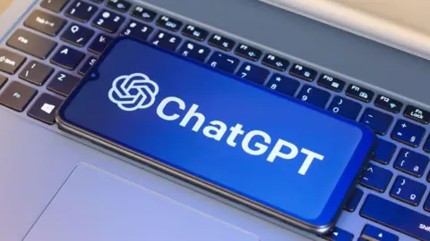 Getty Images A laptop keyboard with a mobile phone on it. On the phone screen is a blue and white ChatGPT logo.